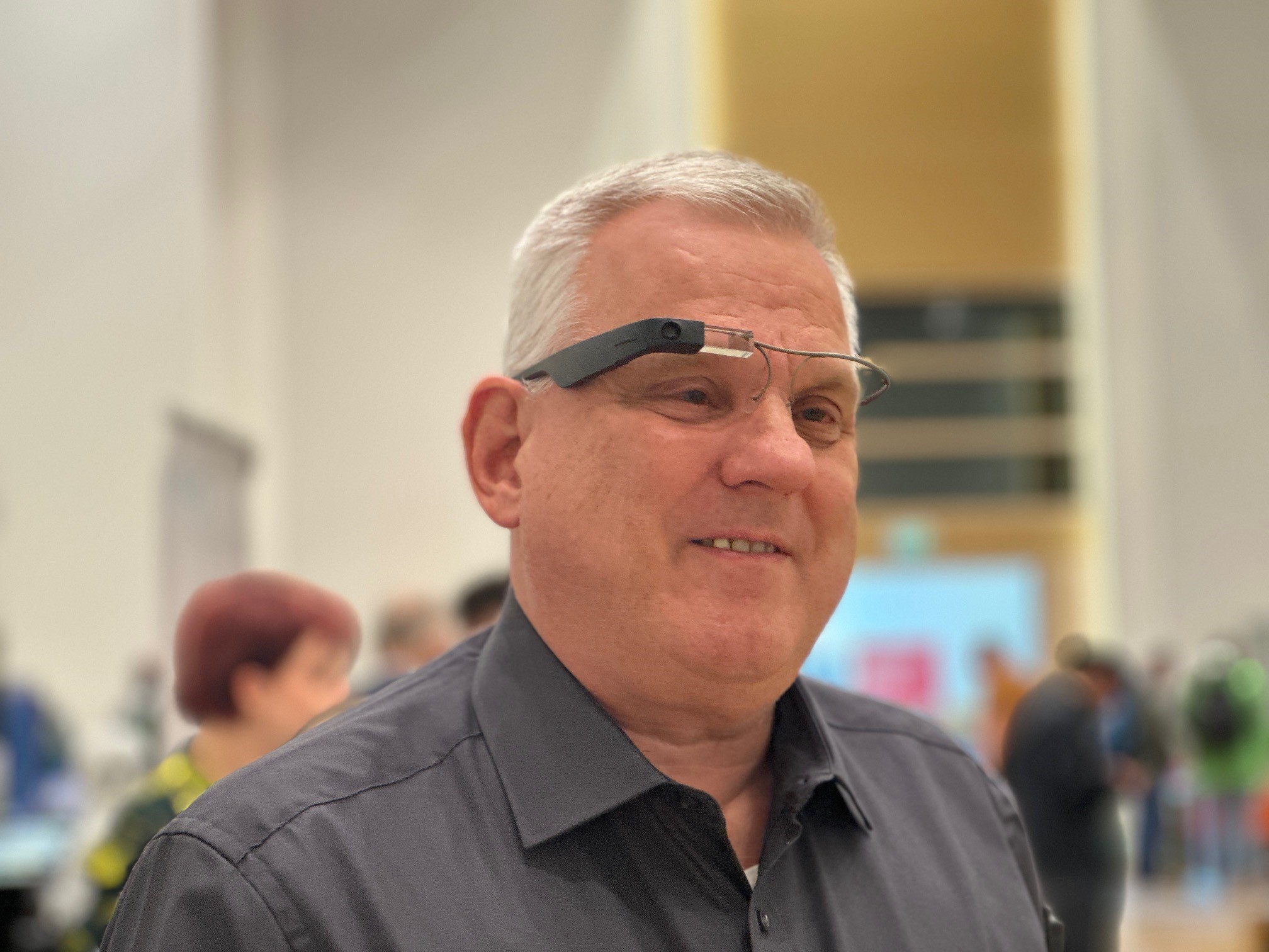 Mann in einem Raum. Er trägt eine Brille an deren rechtem Bügel eine kleine Kamera installiert wurde.