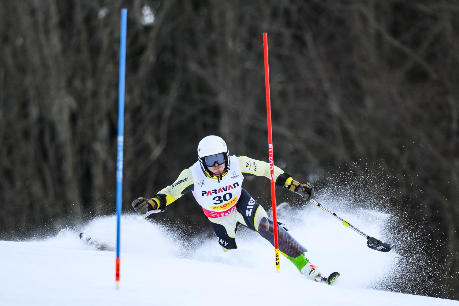 Alpinsportler mit hellem Dress und weißem Helm zwischen einem Tor der Abfahrt im Schnee
