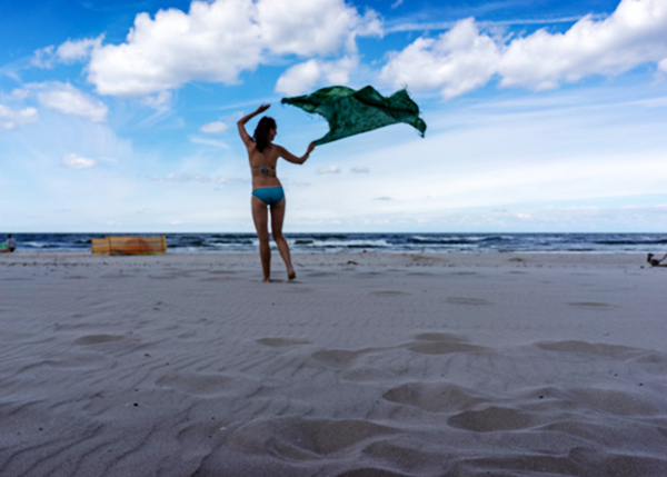 Eine junge Frau am Ostseestrand hält ein im Wind wehendes Tuch
