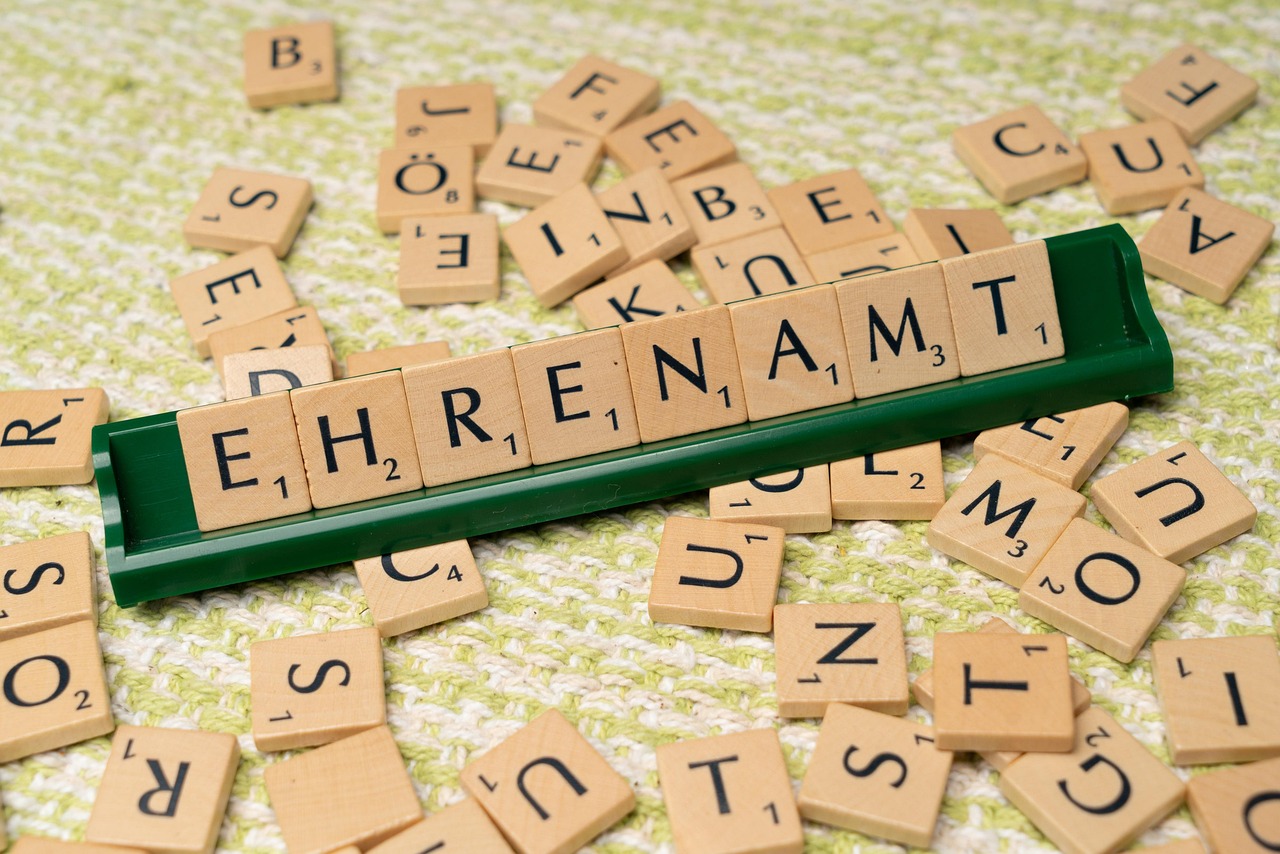Das Wort Ehrenamt auf einer Scrabble-Tafel zusammengestellt. Daneben liegen weitere Buchstaben