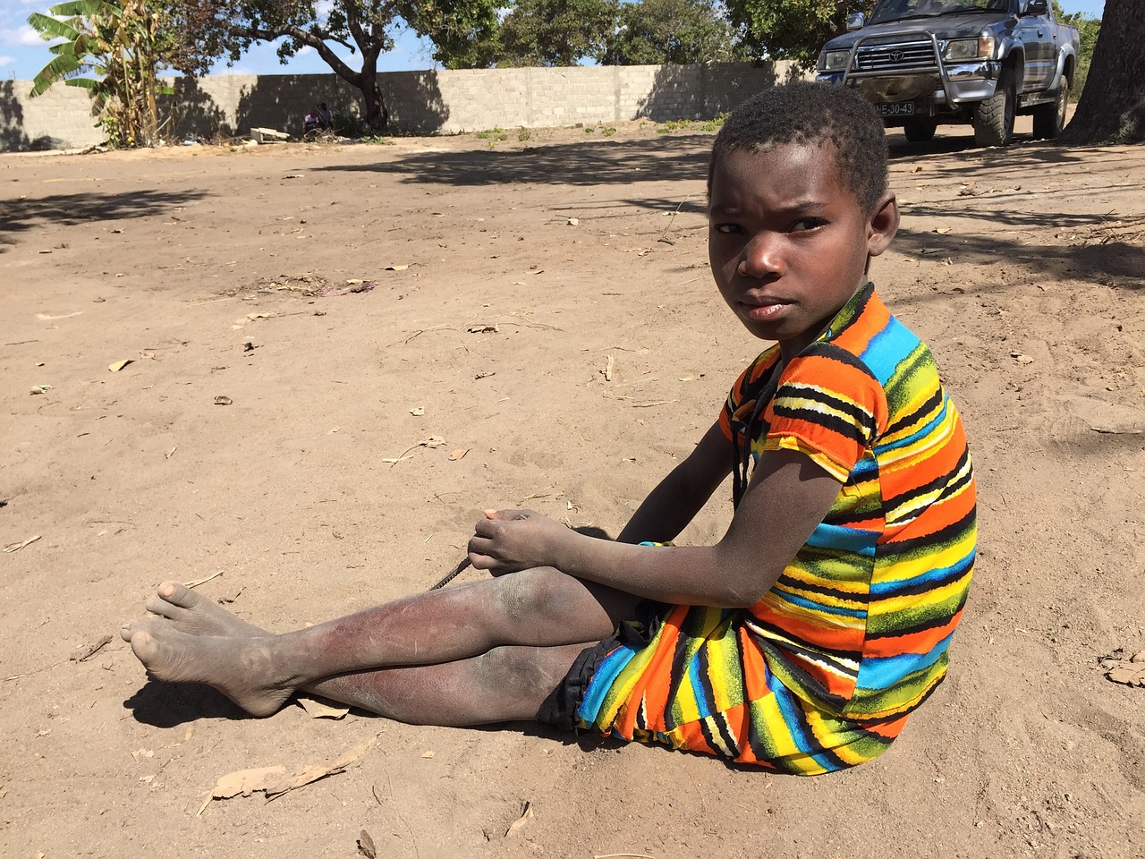 Afrikanisches Mädchen mit bunt gestreiftem Kleid sitz im Sand