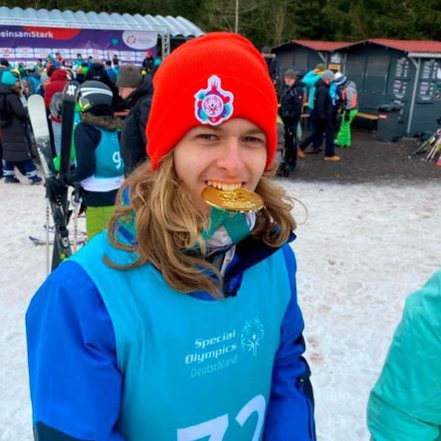 Junger Mann mit langen Haaren im dunkelblauen Sportdress mit hellblauer Veste und roter Pudelmütze