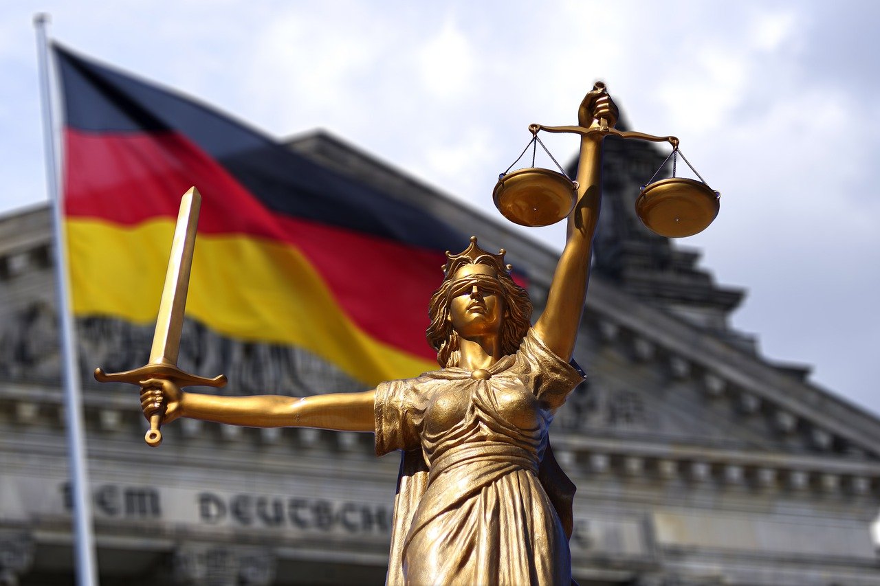 Statue mit Waage und Schwert vor Deutschlandfahne und Reichtagsgebäude