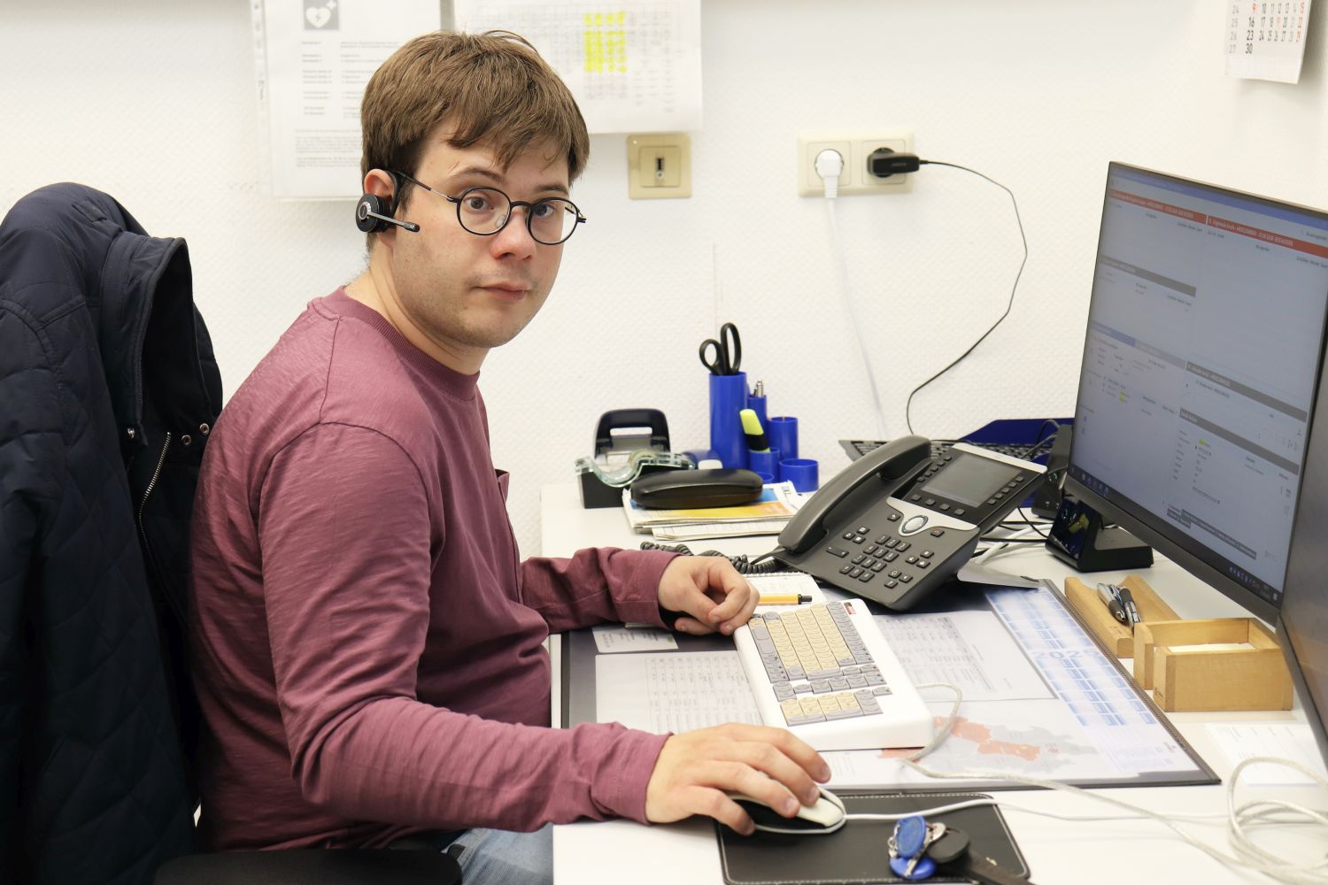 Junger Mann einem Schreibtisch mit Kopfhörern vor einem Computer