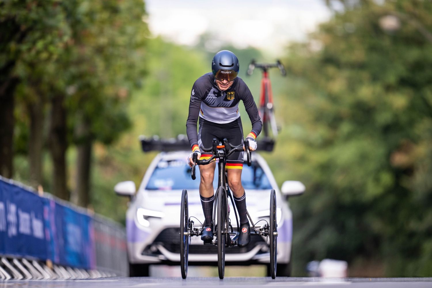 Radsportler mit Helm auf einem Rennrad mit drei Rädern vor einem Polizeiauto