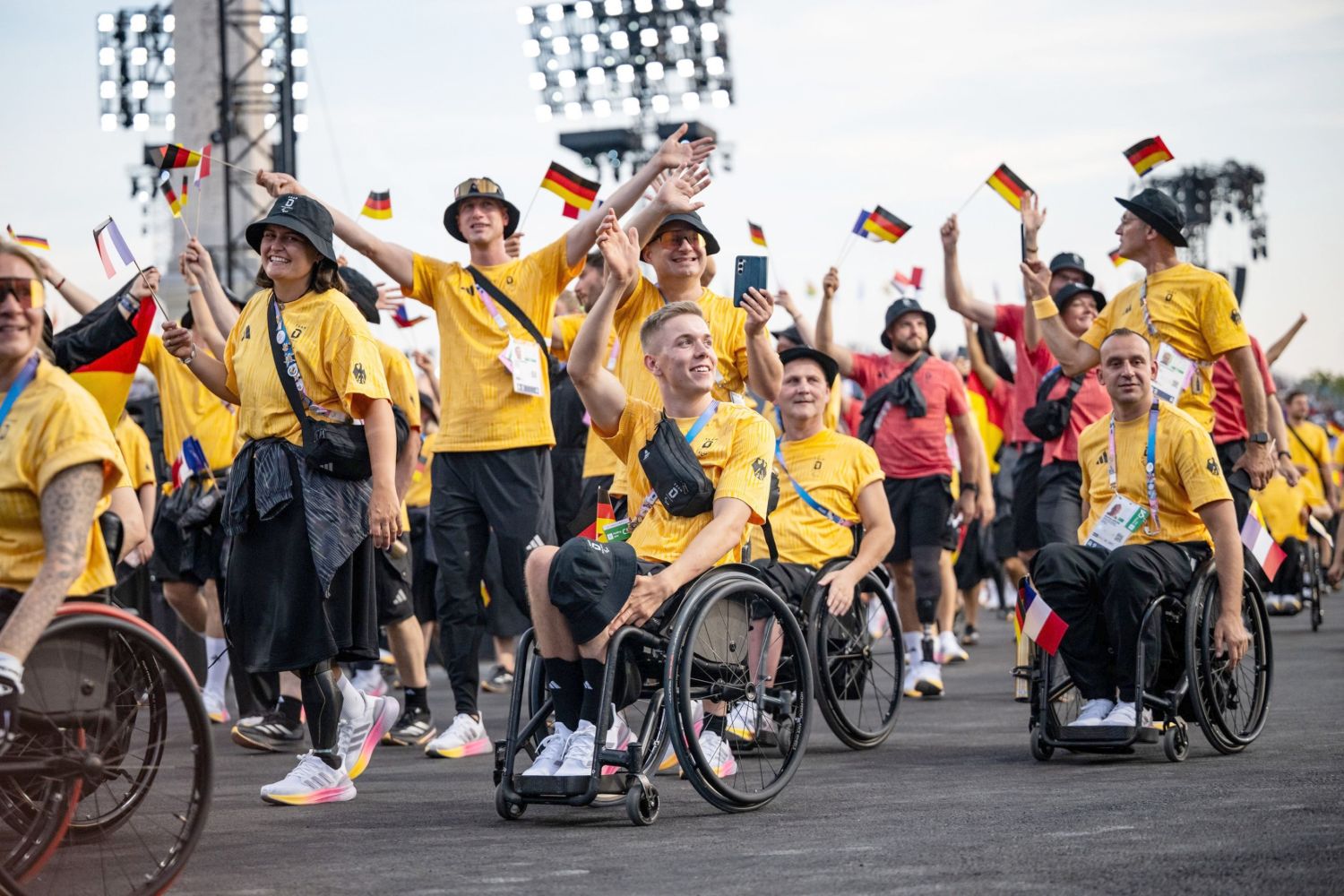 Gruppe von Sportlerinnen und Sportlern in gelbem oder roten Dress laufen vorbei oder passieren mit Rollstuhl