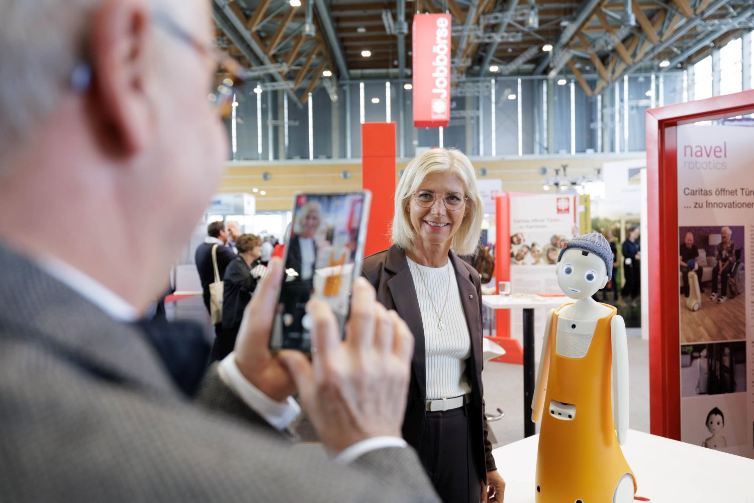 Junge Frau mit blonden Haaren und heller Bluse sowie dunkler Jacke mit Exponaten einer Ausstellung im Hintergrund