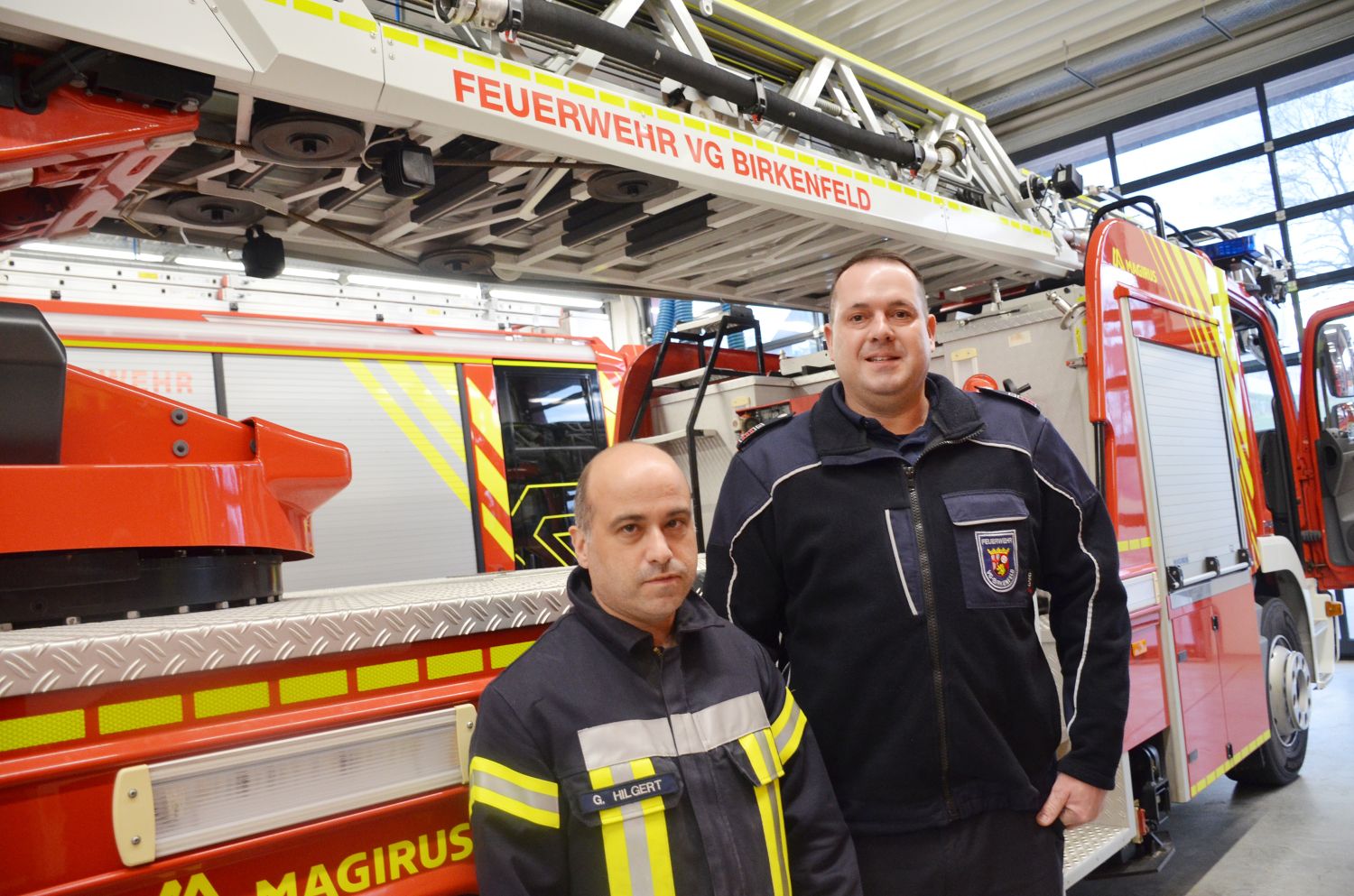 Zwei Männer in Feuerwehruniform vor einem großen Feuerwehrauto
