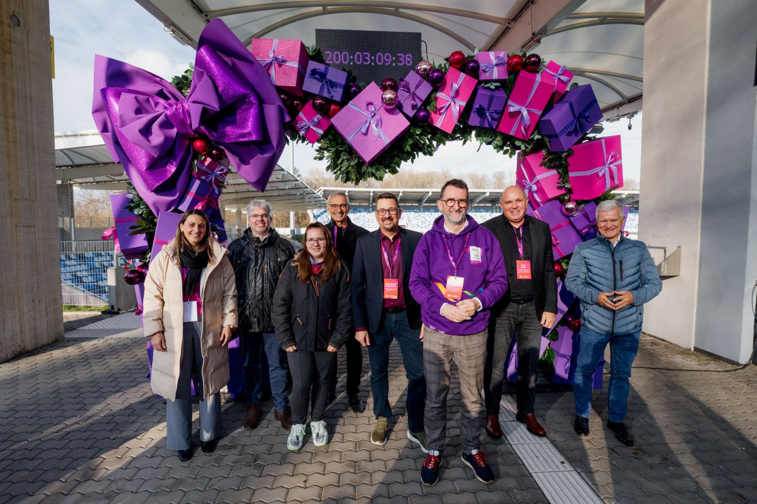 Vor einem großen als Herz gestaltetem Bogen stehen sieben Männer und Frrauen