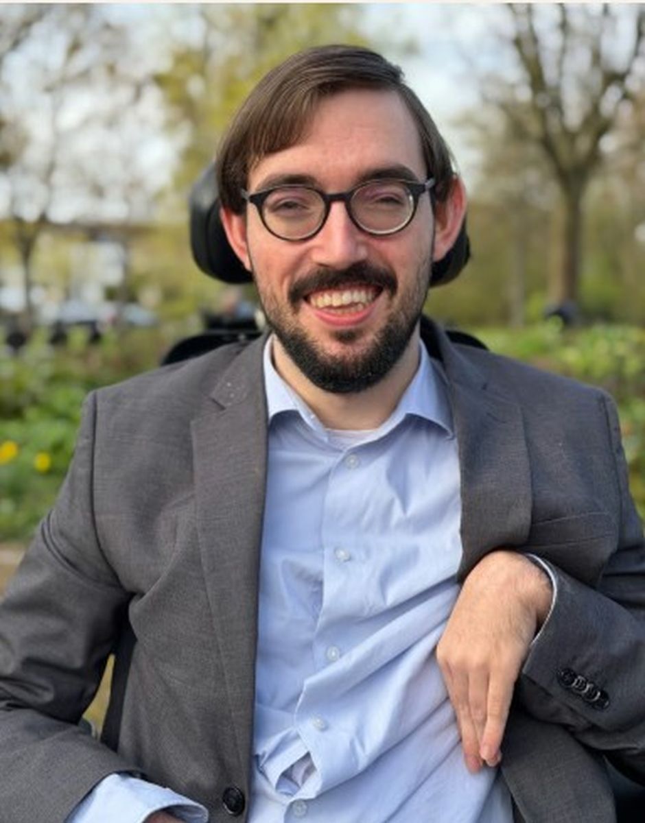 Portrait eines jungen Mannes mit dunklen Haaren Bart und Brille im blauen Hemd und grauem Jacket