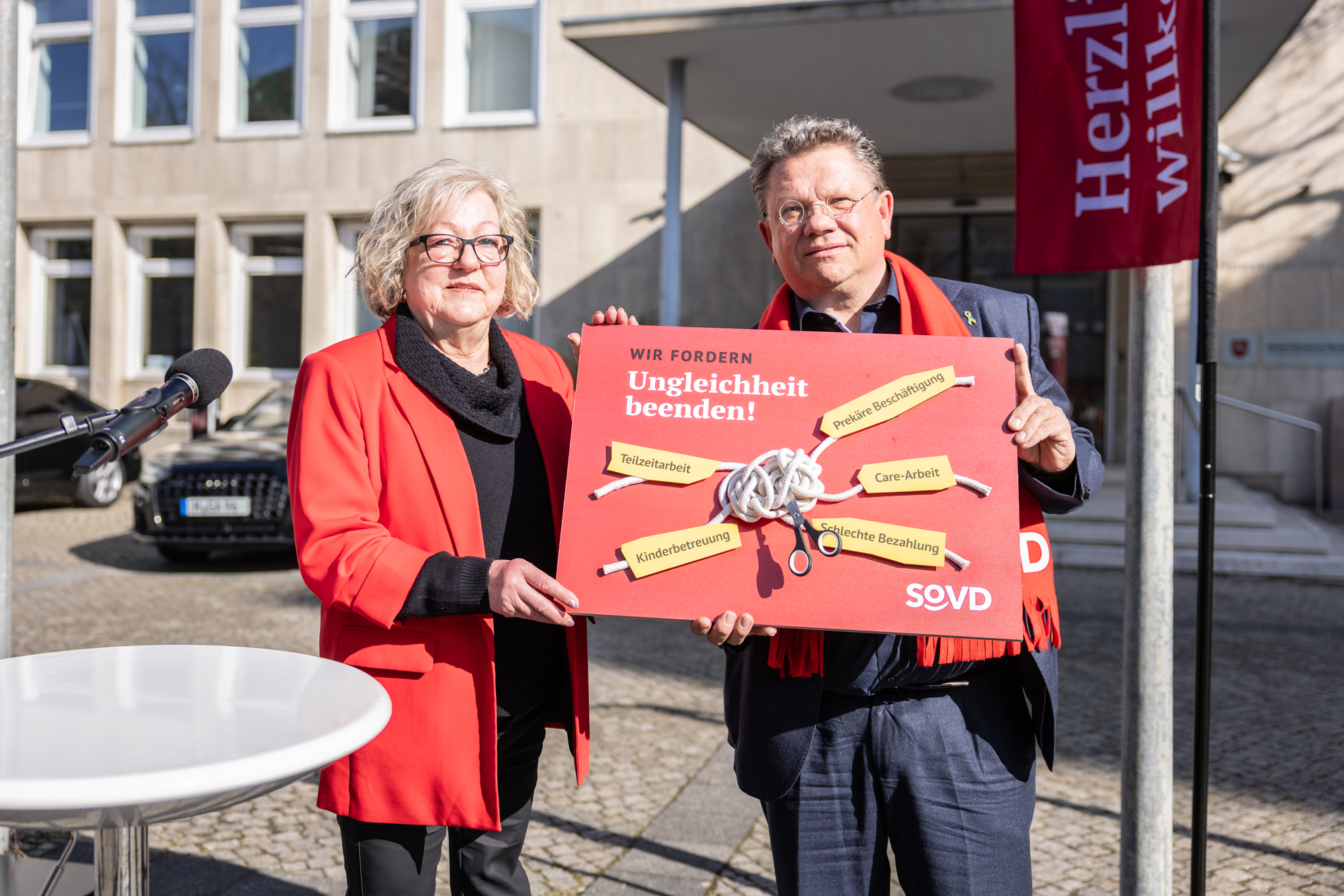 Frau in roter Jacke übergibt rote Tafel mit einem großen Knoten in der Mitte und Tafeln, auf denen die Forderungen stehen und die alle mit dem Knoten verbunden sind.