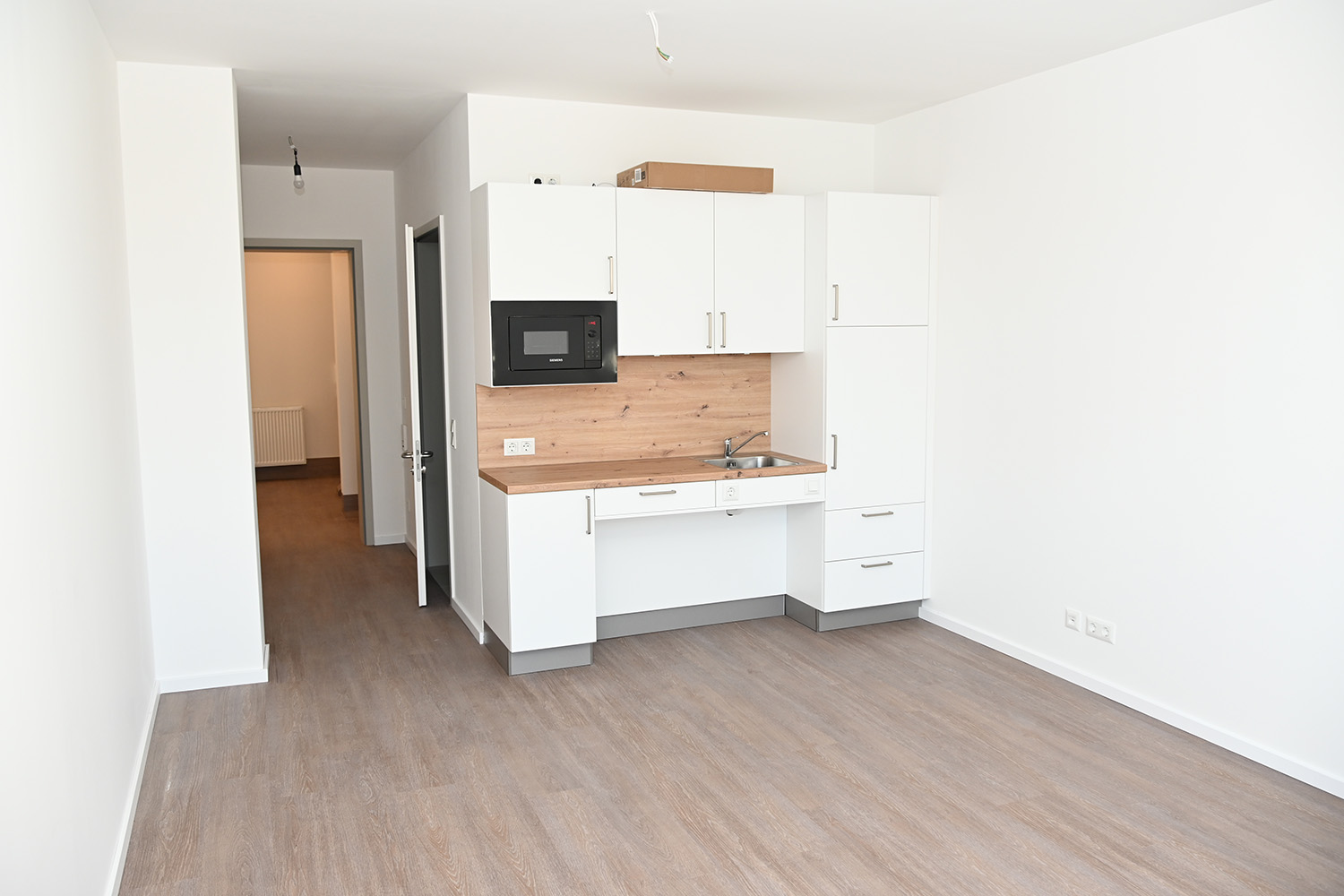 Durchgang in ein weiteres Zimmer, rechts daneben eine kleine Küchenzeilen, davor freier Platz für Tisch und Stühle